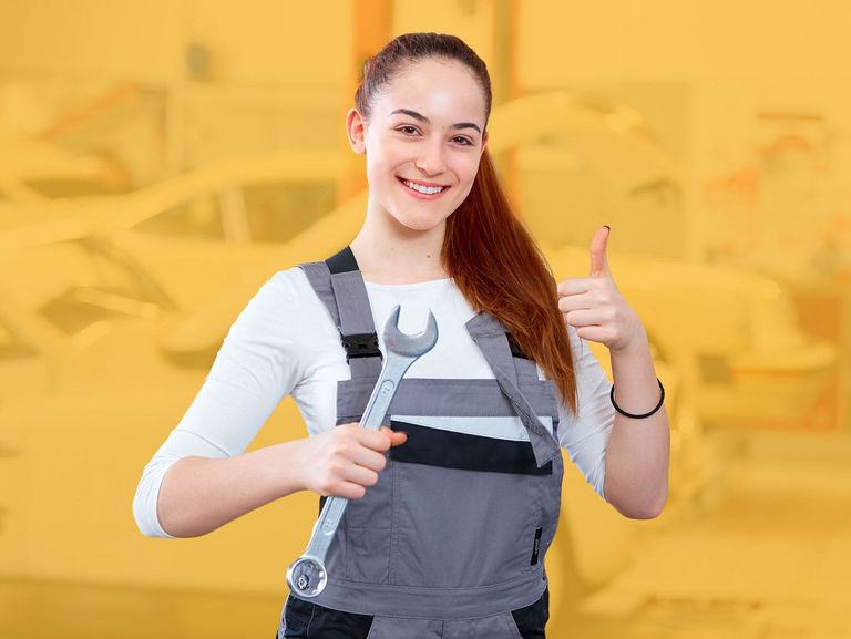 Junge Frau in Werkstatt-Arbeitskleidung mit Schraubenschlüssel