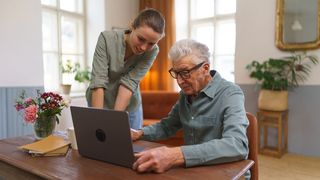 Pflegeanträge Rentner sitzt vor einem Laptop und erhält Hilfe von seiner erwachsenen Enkelin