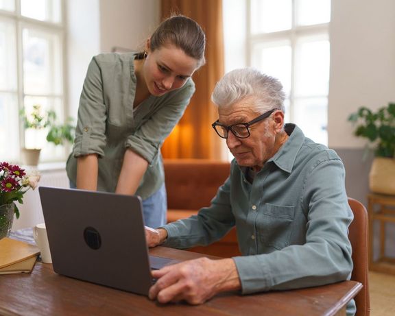 Pflegeanträge Rentner sitzt vor einem Laptop und erhält Hilfe von seiner erwachsenen Enkelin