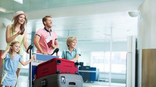 Gesund im Urlaub Vieköpfige Familie fährt schiebt einen Kofferwagen mit Koffern durch ein Flughafengebäude