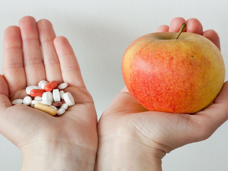 Eine Hand mit Nahrungsergänzungsmittel und eine andere Hand mit einem Apfel
