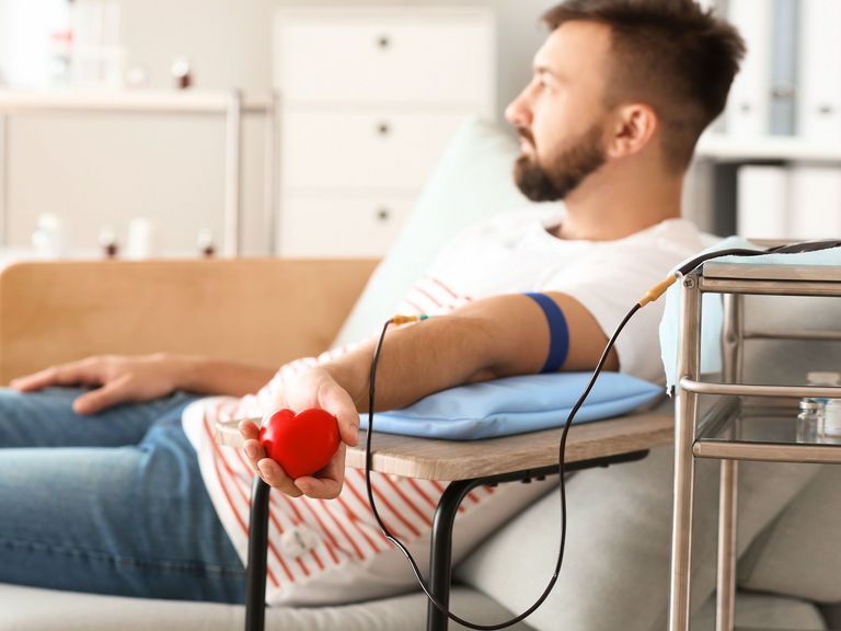 Mann sitzt bei der Blutspende und hält ein rotes kleines Herz in der Hand