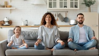Familiäre Entspannung Mutter, Vater und Tochter sitzen im Schneidersitz mit geschlossenen Augen auf einem Sofa und entspannen