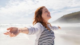 Bewusstes Atmen Frau mit ausgebreiteten Armen und einem Lächeln im Gesicht genießt die Meeresluft am Strand
