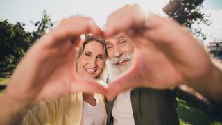 Herzwoche Älteres Paar lacht, formt mit den Händen ein Herz und schaut hindurch