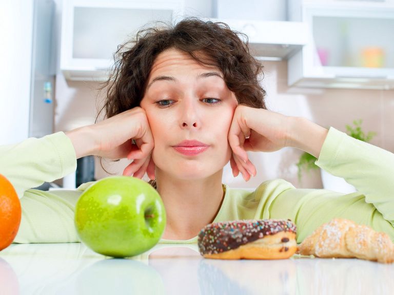 Junge Frau wählt zwischen Orange, Apfel und Süßigkeiten