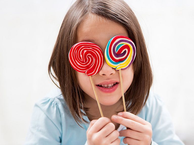 Kleines Mädchen hält sich zwei bunte Lutscher vor die Augen