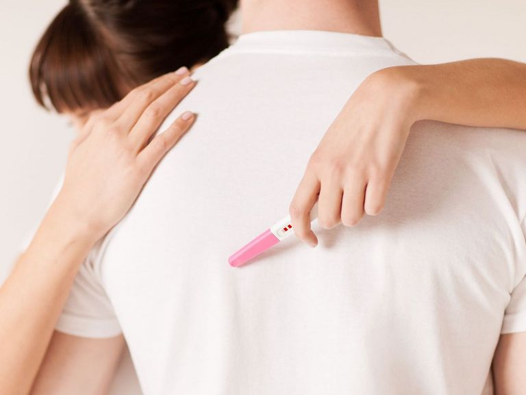 Frau mit einem Schwangerschaftstest in der Hand im Arm eines Mannes