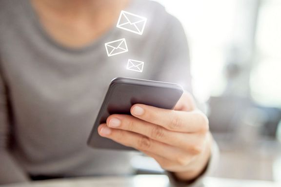 Gesundheitsnewsletter Frauenhand hält ein Smartphone und darüber schweben kleine Briefumschlagsymbole