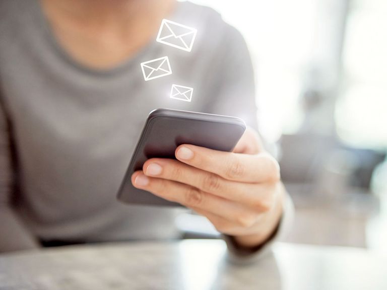 Frauenhand hält ein Smartphone und darüber schweben kleine Briefumschlagsymbole