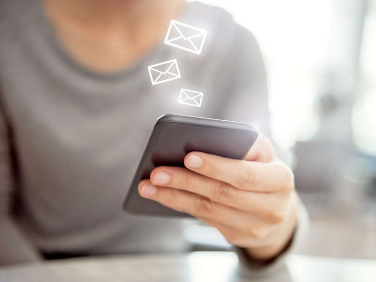 Frauenhand hält ein Smartphone und darüber schweben kleine Briefumschlagsymbole