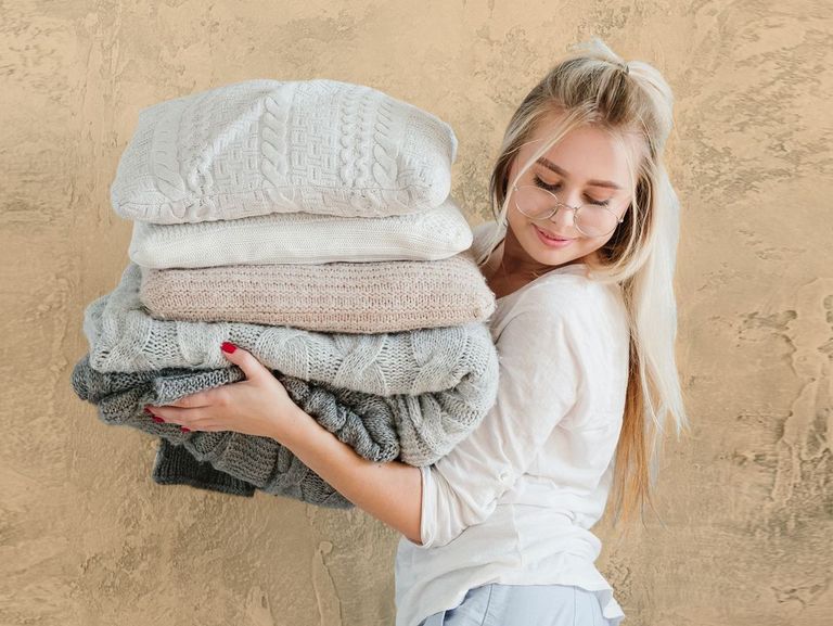  	Blonde Jugendliche trägt einen Stapel Kissen vor sich und schaut auf den Boden neben sich 