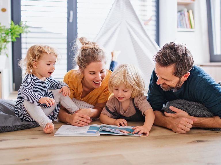 Familie mit 2 Kindern lesen im Kinderzimmer auf dem Fußboden gemeinsam mit viel Freude ein Buch