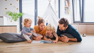 Familie mit 2 Kindern lesen im Kinderzimmer auf dem Fußboden gemeinsam mit viel Freude ein Buch