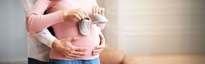 Mann hält den Babybauch einer Frau und diese hat Babyschuhe in der Hand