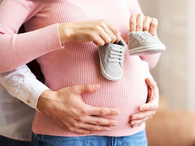 Mann hält den Babybauch einer Frau und diese hat Babyschuhe in der Hand