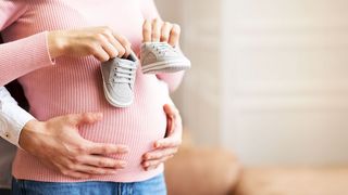 BabyStartPlus-Beratung Mann hält den Babybauch einer Frau und diese hat Babyschuhe in der Hand