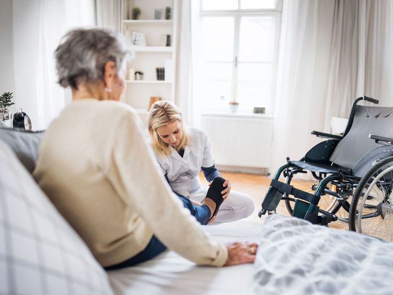 Pflegende hilft einer Pflegebedürftigen beim Schuhe anziehen