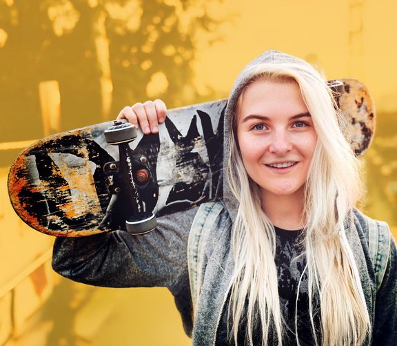 Junge blonde Frau mit Skateboard über der Schulter