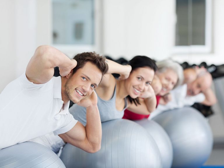 Männer und Frauen liegen bäuchlings auf Gymnastikbällen und haben die Händen hinter dem Kopf verschränkt