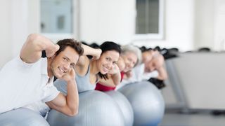 Männer und Frauen liegen bäuchlings auf Gymnastikbällen und haben die Händen hinter dem Kopf verschränkt