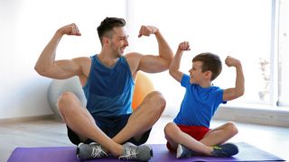 Muskelarbeit Vater und Sohn zeigen im Schneidersitz sitzend ihr Armmuskeln