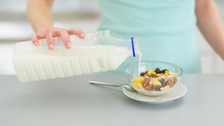 Frau gießt Milch über ihr Müsli