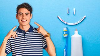 Zahngesundheit Junger Teenager zeigt auf seine Zähne mit Zahnpasta und Zahnbürste im Bildhintergrund