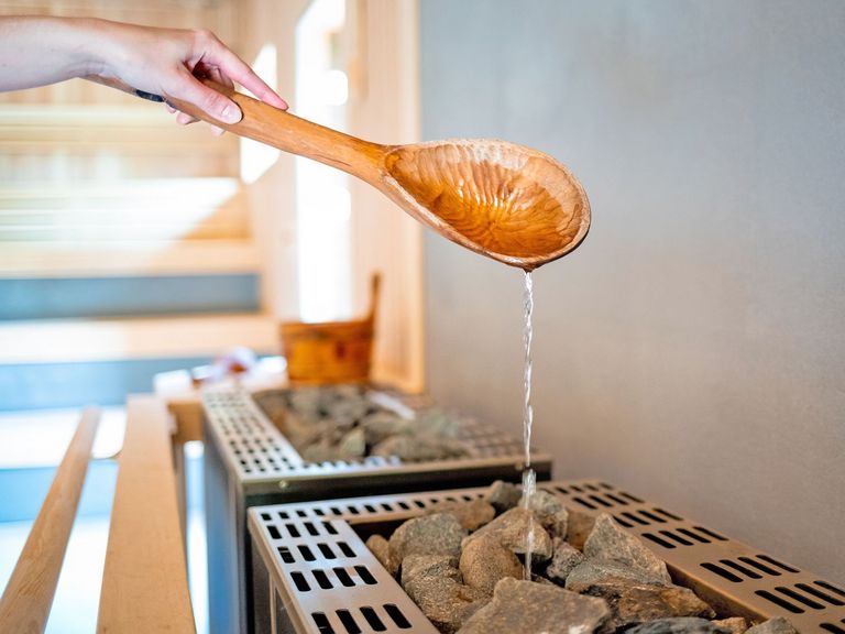 Großer Holzlöffel in einer Sauna, von dem Wasser herunterläuft