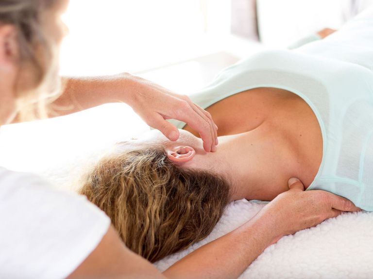 Frau liegt auf dem Rücken auf einer Liege und wird mit Akupressur am Hals und Nacken behandelt