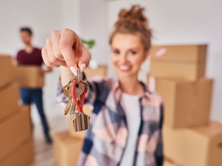 Junge Frau mit Umzugskartons zeigt Schlüssel in die Kamera﻿