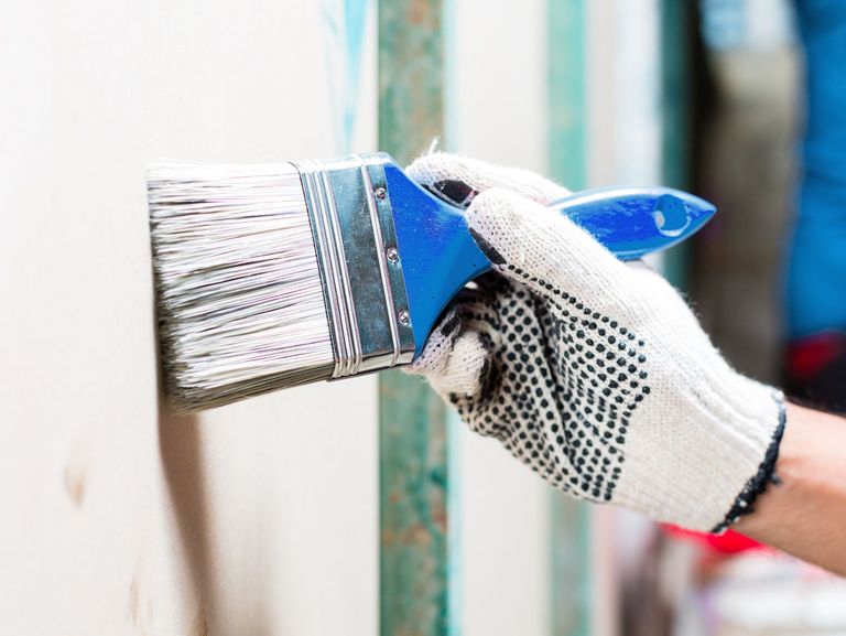 Maler trägt bei Malerarbeiten Schutzhandschuhe