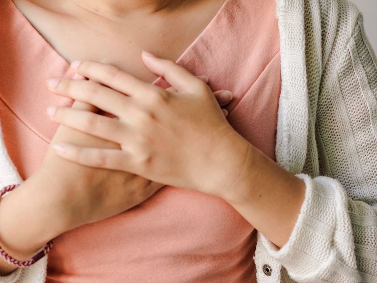 Frau hält wegen Schluckauf beide Hände übereinander auf dem Brustkorb