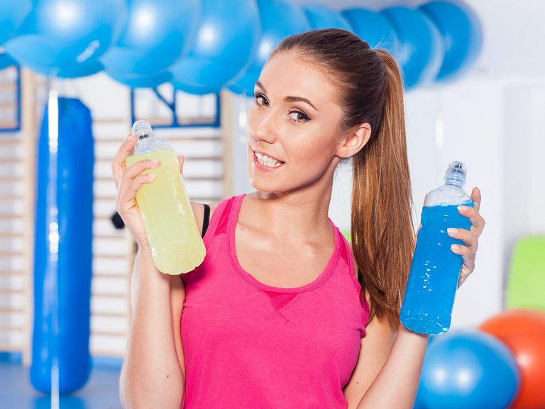 Frau im Sportdress hält zwei Flaschen mit isotonischen Getränken