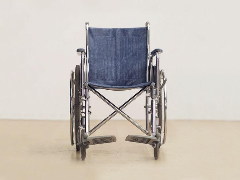 ein leerer Rollstuhl vor eine weißen Wand