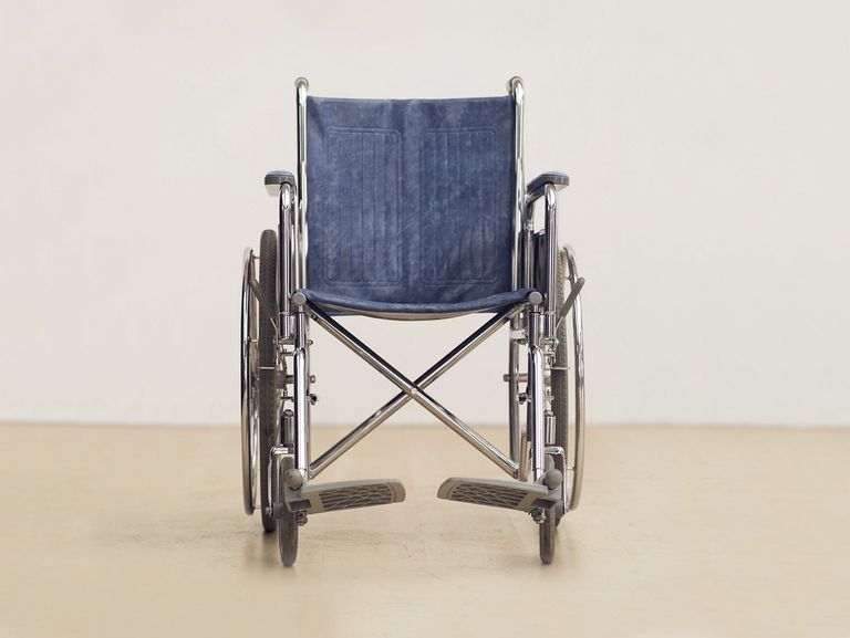 ein leerer Rollstuhl vor eine weißen Wand