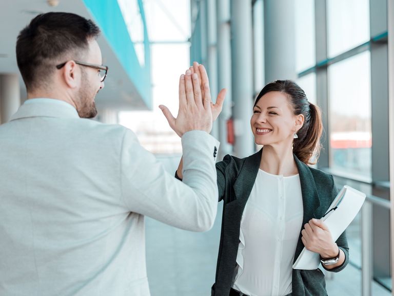 Zwei Bürokollegen klatschen sich fröhlich lachend ab