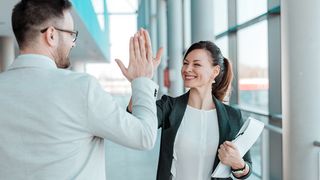 Zwei Bürokollegen klatschen sich fröhlich lachend ab