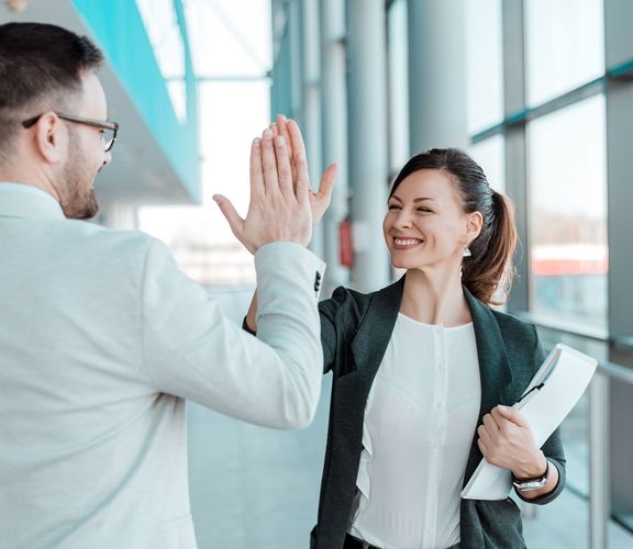 Zwei Bürokollegen klatschen sich fröhlich lachend ab