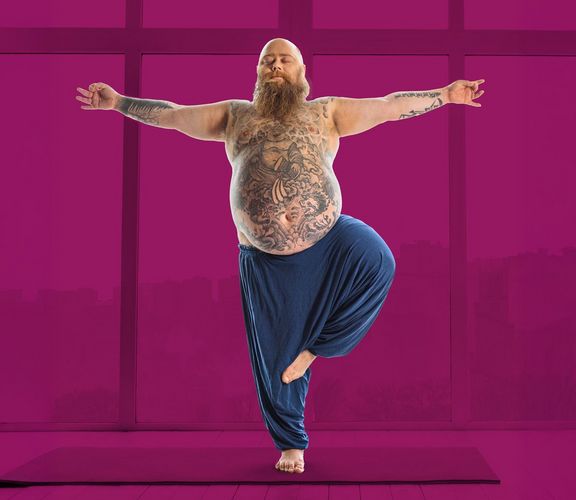 Gelassenheitspaket Bärtiger Mann mit Bauch und Tattoos balanciert auf einem Bein, Arme ausgestreckt