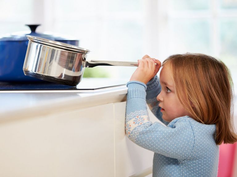 Kleines Kind will einen heißen Topf vom Herd ziehen