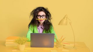 Junge Frau mit Brille und zerzausten Haaren am Schreibtisch mit Laptop