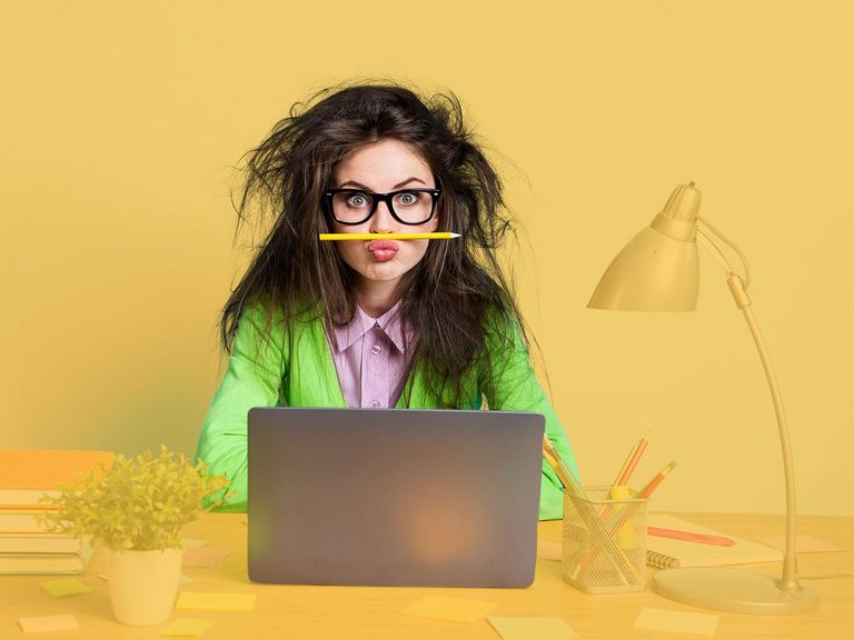 Junge Frau mit Brille und zerzausten Haaren am Schreibtisch mit Laptop