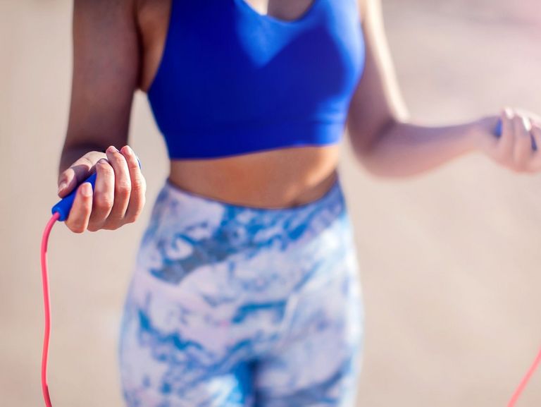 Sportlerin in blauer Kleidung hält ein Springseil in den Händen