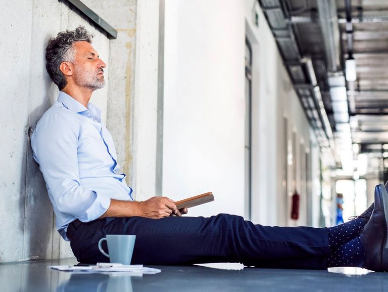 Mann sitzt mit geschlossenen Augen an einer Wand und macht Pause