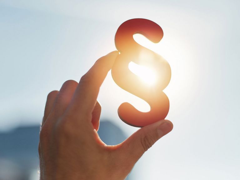 Eine Hand hält ein Paragraphenzeichen in die Sonne