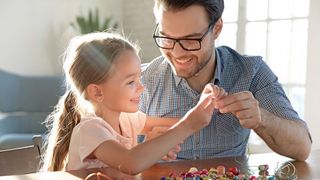 Glücklicher Vater fädelt mit seiner kleinen Tochter bunte Perlen auf einen Faden