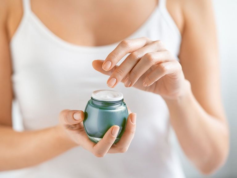 Frau hält einen geöffneten Tigel mit Hautcreme in die Kamera