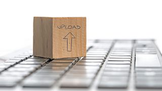 Laptoptastatur und darauf ein kleiner Holzblock mit der Aufschrift "Upload"