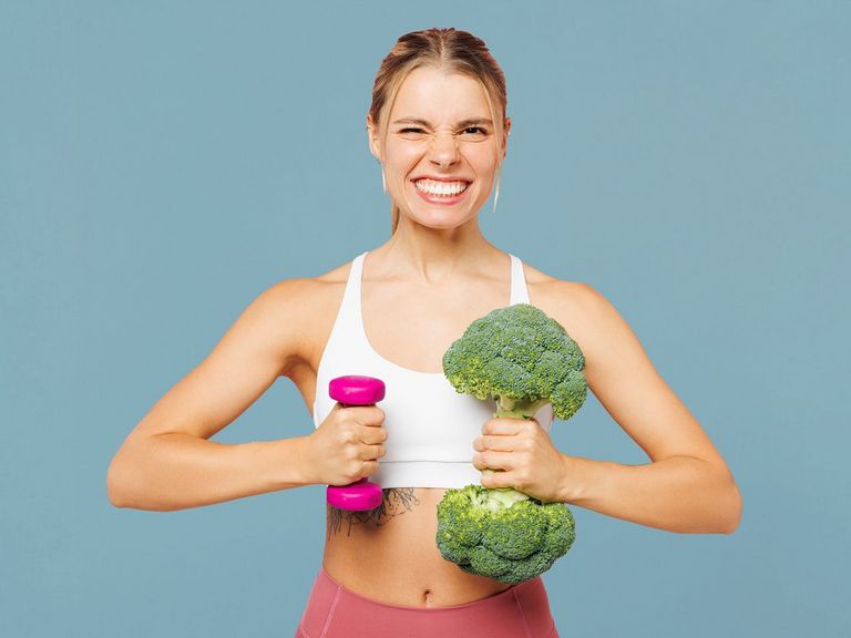 Sportlerin mit einer Hantel in der einen Hand und einem Brokkoli in der anderen Hand